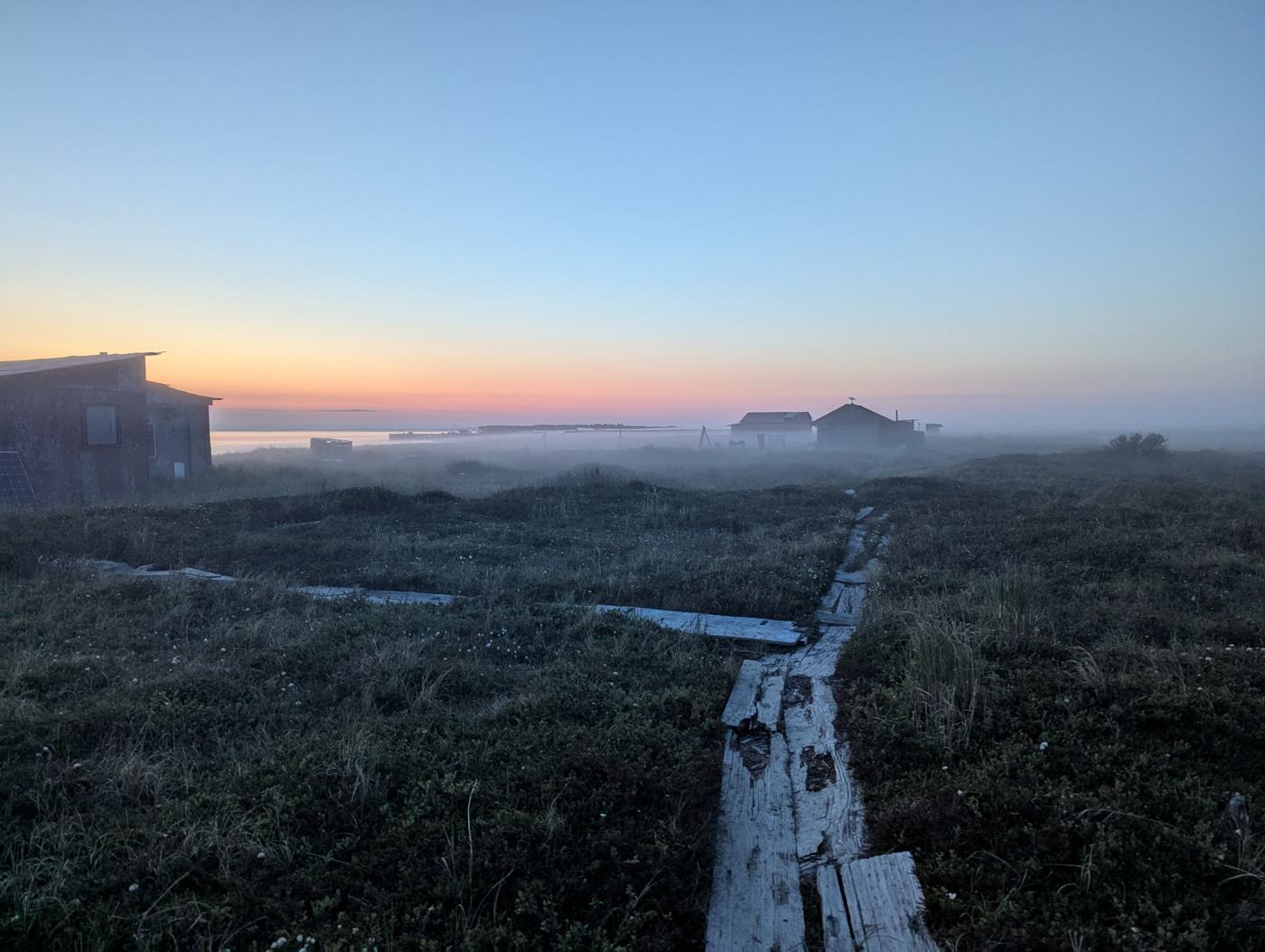 Boardwalk through tundra toward fish camp cabins in fog